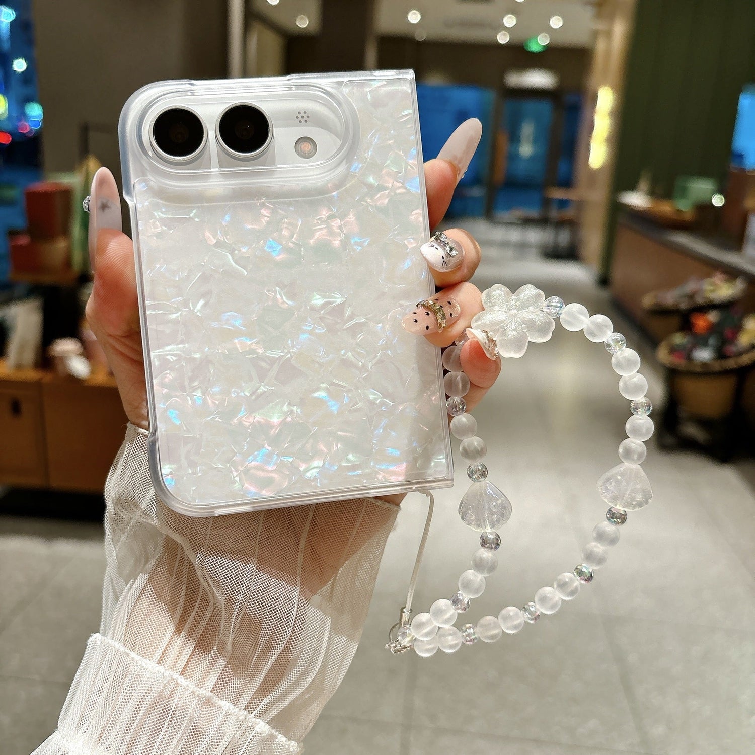 iPhone Duo pearl shell case with beaded wrist strap held in hand